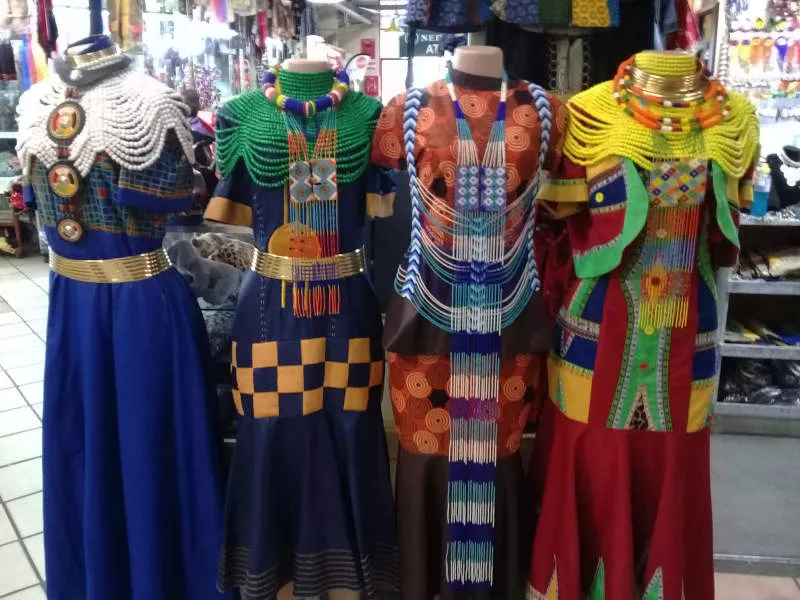 Four colourful dresses with traditional necklace bead work are displayed in a row.