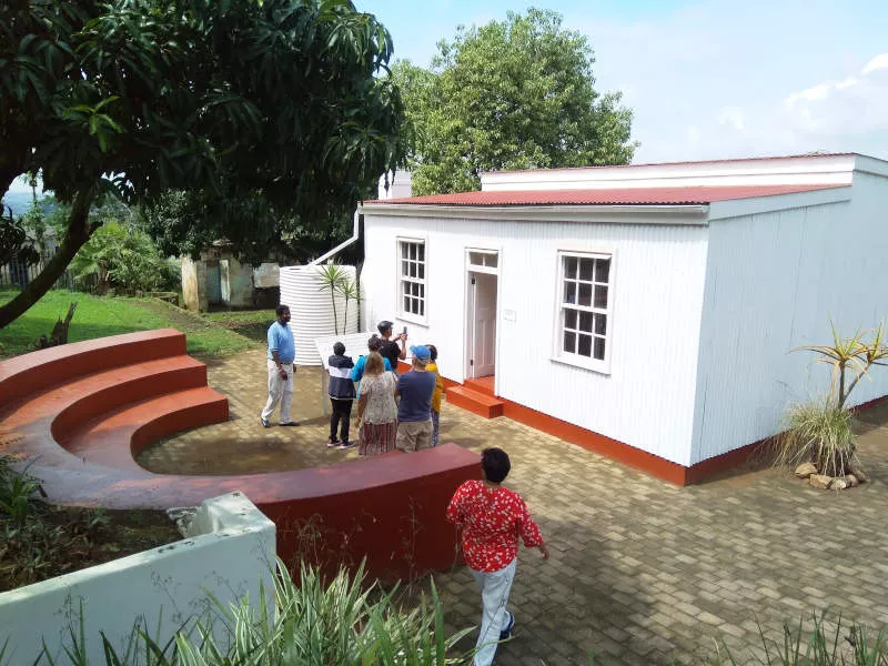 A group of people or different races stand in front of a corrugated iron building that is painted white.