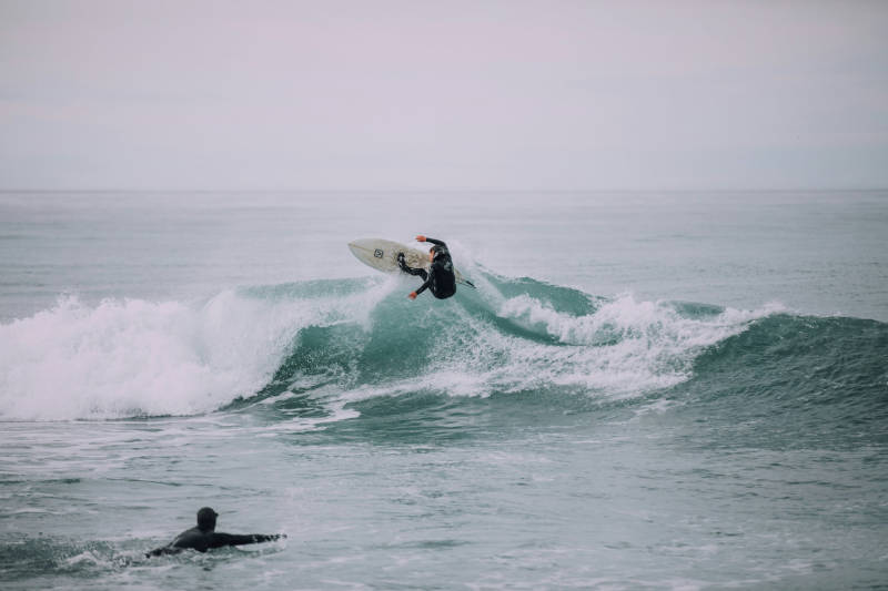 A surfer rides a wave while another surfer paddles out