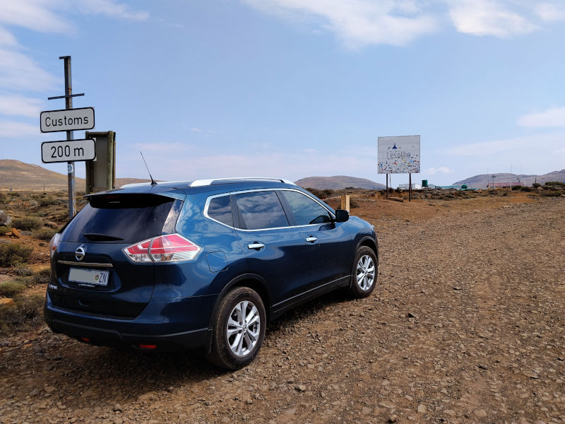A blue Toyota Xtrail is parked in front of a sign that says "customs Lesotho"